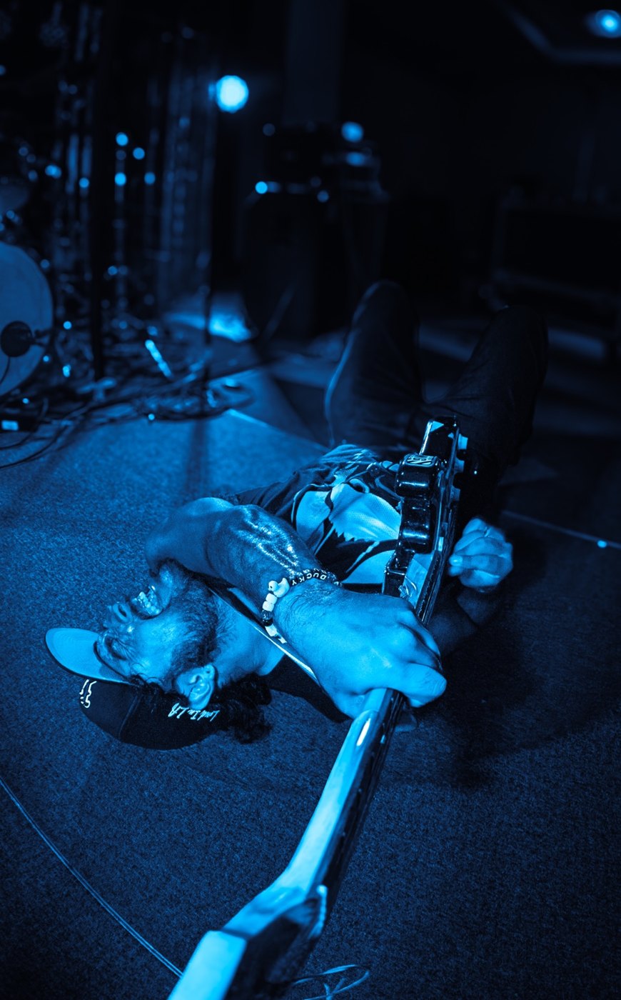 Musician lying onstage under blue lights with a guitar